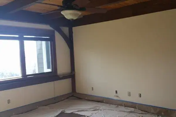 Room with fresh cream walls and dark wood trim, the floor still under drop cloths and tape
